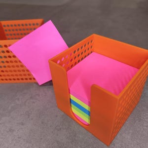 Peut inclure: Organiseur de bureau en plastique orange avec un motif en grille. L'organisateur contient une pile de notes autocollantes roses, vertes, jaunes et bleues.