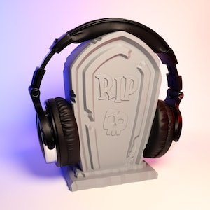 May include: A black headphone stand shaped like a tombstone with the words "RIP" and a skull on the front.