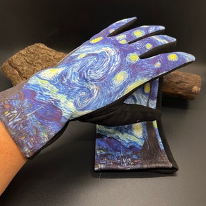 May include: A pair of gardening gloves featuring a print of Van Gogh's "Starry Night" painting. The gloves have a black palm and fingers, with a gray cuff. The artwork depicts swirling blue and yellow brushstrokes, with a village scene at the bottom.