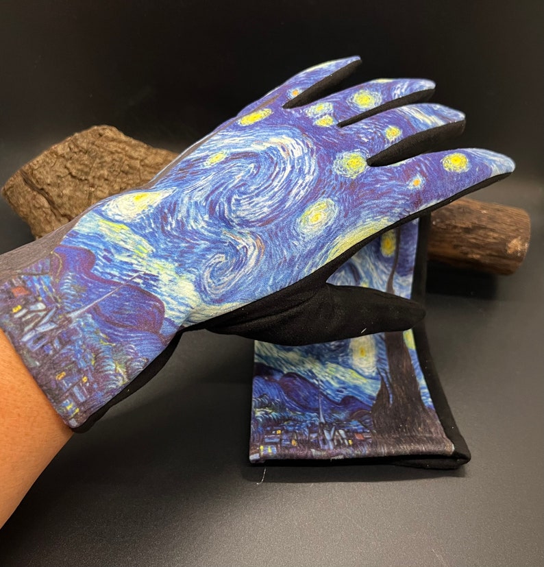 May include: A pair of gardening gloves featuring a print of Van Gogh's "Starry Night" painting. The gloves have a black palm and fingers, with a gray cuff. The artwork depicts swirling blue and yellow brushstrokes, with a village scene at the bottom.