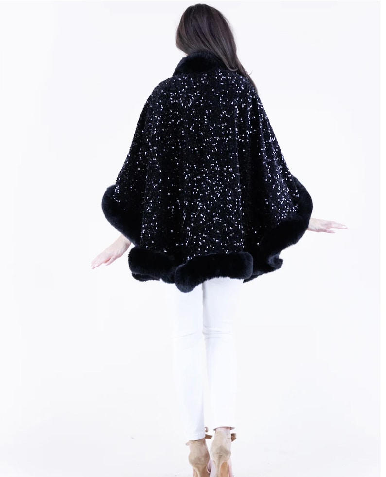 May include: A black sequined cape with a fur trim. The cape is worn by a person with long dark hair and white pants.