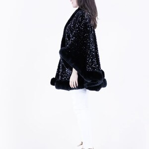 May include: A black sequined cape with a fur trim. The cape is worn by a person standing on a white background.