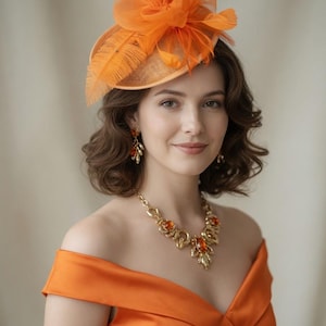 May include: An orange fascinator with feathers and a matching orange dress. The hat features a mesh and feather design. A gold necklace with orange gemstones and matching earrings complete the look. The dress has an off-the-shoulder neckline.