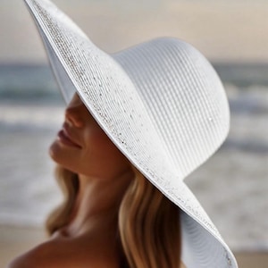May include: A wide-brimmed white sun hat with a textured weave. The hat has a gently curved brim and a rounded crown. The hat is worn by a person with blonde hair, with the beach and ocean in the background.