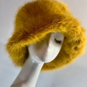 Könnte beinhalten: Ein gelber Eimerhut aus Kunstfell. Der Hut ist weich und flauschig und hat einen breiten Rand.