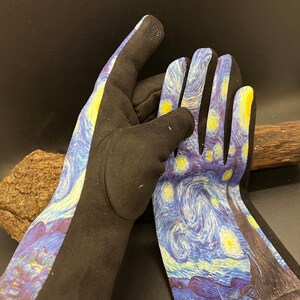 May include: A pair of gardening gloves featuring a print of Van Gogh's "Starry Night" painting. The gloves have a black palm and fingers, with the artwork covering the back of the hand and wrist area. The artwork includes yellow stars and a blue night sky.