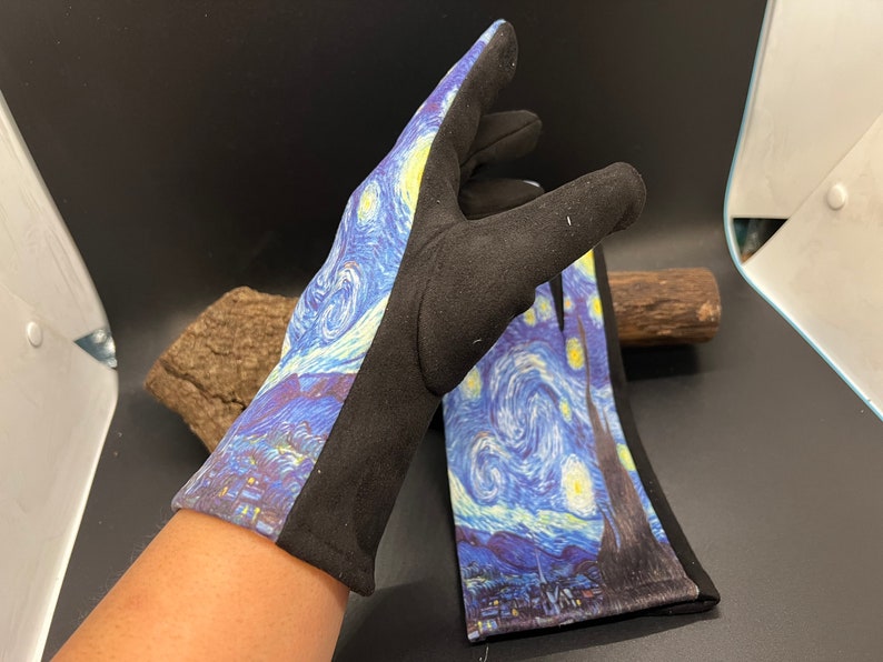 May include: A pair of black gloves with a print of Van Gogh's "Starry Night" painting. The gloves feature a black cuff and a black side panel. The artwork depicts a swirling blue night sky with yellow stars and a village.