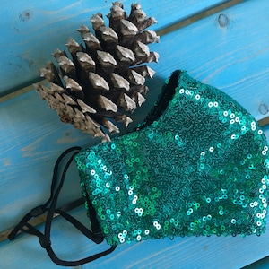 May include: A teal green face mask with sequins. The mask has black elastic straps.