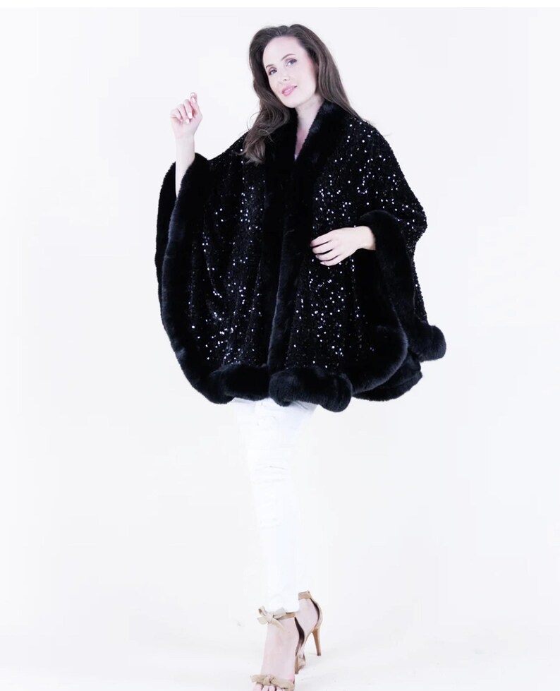 May include: A black sequined cape with a fur trim. The cape is worn by a model with white pants and heels.