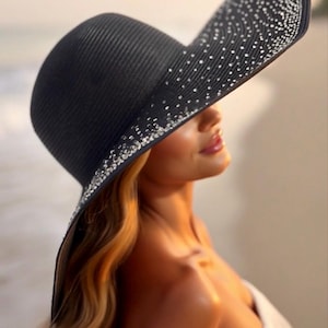 May include: A black sun hat with a wide brim, adorned with sparkling embellishments along the edge. The hat has a textured surface and is angled, casting a shadow. The hat is a fashion accessory.