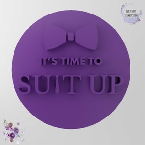May include: Purple round cookie cutter with the text "It's time to suit up" and a bow tie design.