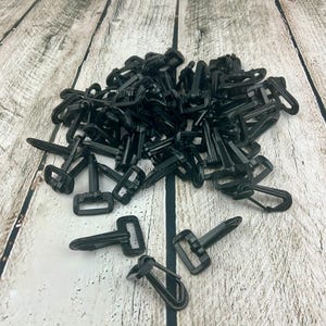 May include: A pile of black plastic swivel hooks. The hooks are designed to be used with webbing or straps.