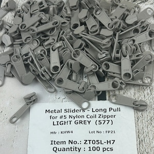 May include: A pile of 100 light grey metal zipper sliders with long pulls. The sliders are for #5 nylon coil zippers. The text on the label reads: "Metal Sliders - Long Pull for #5 Nylon Coil Zipper LIGHT GREY (577) Mfr: KHW4 Lot No: FP21 Item No.: ZT05L-H7 Quantity: 100 pcs"