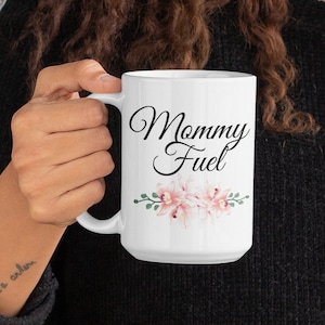 May include: White ceramic coffee mug with the text "Mommy Fuel" in black script with pink floral accents.
