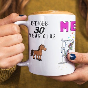 May include: White ceramic mug with a black handle. The mug has a graphic of a unicorn on a pole and the text "Other 30 year olds Me". There is also a graphic of a brown horse on the mug.