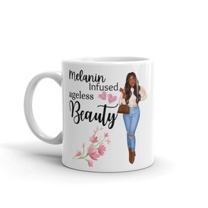 May include: White ceramic mug with a black and white illustration of a woman with brown hair and a white shirt and blue jeans. The text "Melanin Infused ageless Beauty" is printed on the mug with pink hearts and pink flowers.