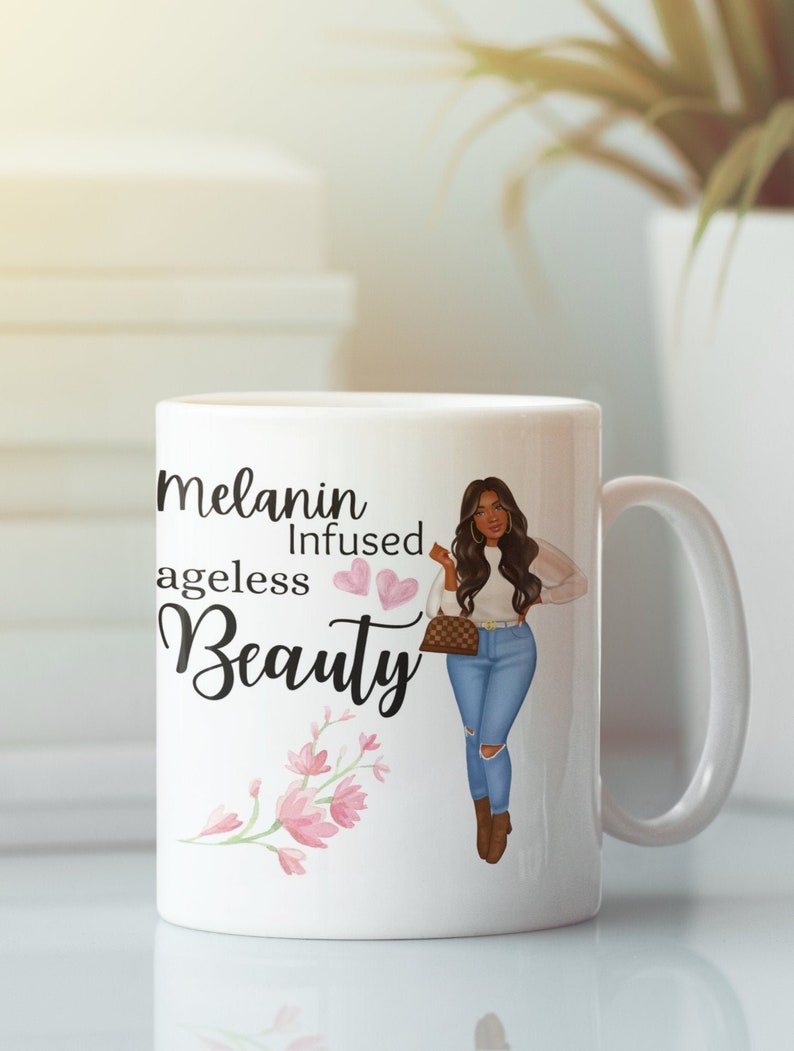 May include: White ceramic mug with a black and white illustration of a woman with long dark hair, wearing a white sweater, blue jeans, and brown boots. The mug has the text "Melanin Infused Ageless Beauty" with two pink hearts and a pink floral design.