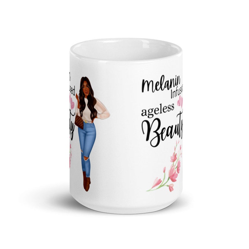 May include: White ceramic mug with a black and white illustration of a woman with brown hair and a pink floral design. The text "melanin infused ageless beauty" is printed on the mug.