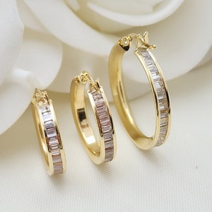 May include: Three gold hoop earrings with a row of clear baguette-shaped stones around the edge.