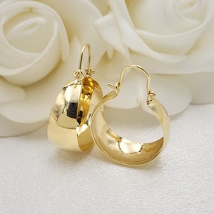 Könnte beinhalten: Ein Paar goldene Creolen. Die Ohrringe sind dick und haben eine abgerundete Form.
