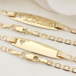 K&ouml;nnte beinhalten: Drei goldene Armb&auml;nder mit einem herzf&ouml;rmigen Ausschnitt auf dem Namensschild. Der Name "Linda" ist auf dem oberen Namensschild graviert. Die Armb&auml;nder bestehen aus einer dreifarbigen Kette mit Gold, Ros&eacute;gold und Wei&szlig;gold.
