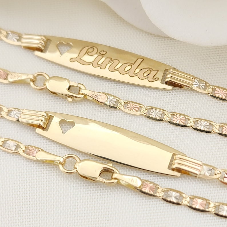 K&ouml;nnte beinhalten: Drei goldene Armb&auml;nder mit einem herzf&ouml;rmigen Ausschnitt auf dem Namensschild. Der Name "Linda" ist auf dem oberen Namensschild graviert. Die Armb&auml;nder bestehen aus einer dreifarbigen Kette mit Gold, Ros&eacute;gold und Wei&szlig;gold.