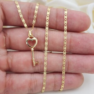 May include: A gold heart-shaped key pendant necklace with a delicate chain. The chain is made of small, linked squares with a textured finish.