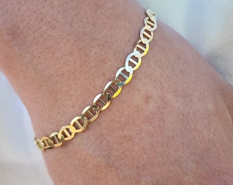 May include: A gold chain bracelet with a mariner link design. The bracelet is on a person's wrist.