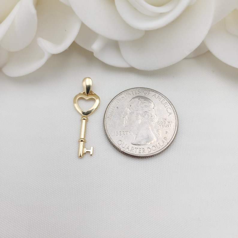 May include: A gold-colored key charm with a heart-shaped keyhole. The charm is about the size of a US quarter.