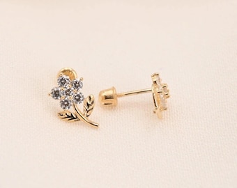 May include: A pair of gold-colored flower stud earrings. Each earring features a flower design with small, clear stones in the center and a delicate leaf and stem detail. The earrings are set against a soft, off-white background.