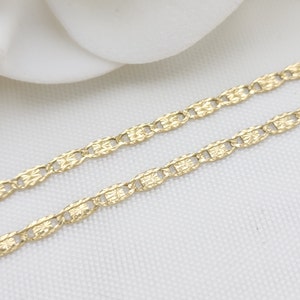 May include: A gold chain necklace with a delicate, patterned design. The chain is made of small, linked oval shapes with a textured surface.