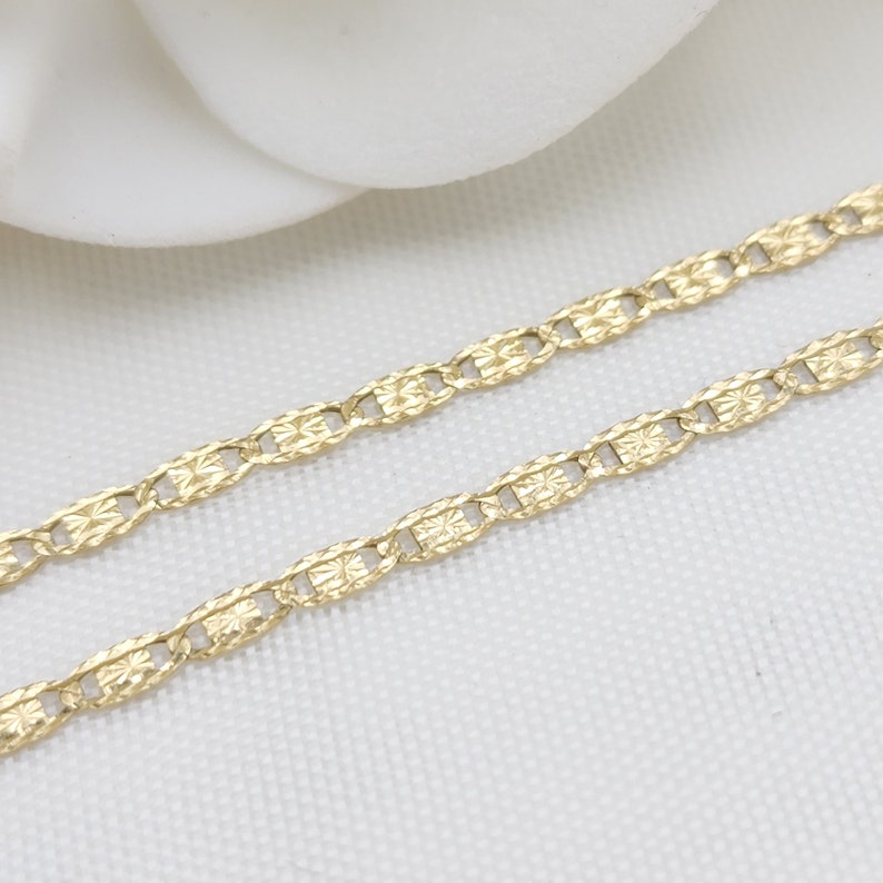 May include: A gold chain necklace with a delicate, patterned design. The chain is made of small, linked oval shapes with a textured surface.