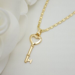 May include: A gold heart-shaped key pendant necklace with a delicate chain. The key has a simple design with a heart-shaped bow at the top and a small, round knob at the bottom.