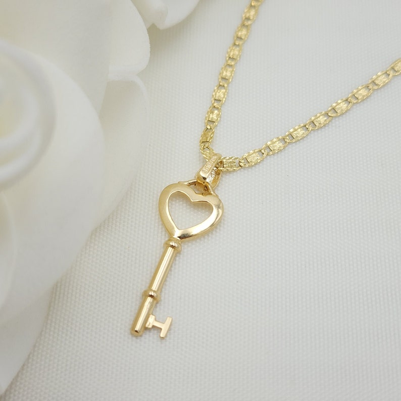 May include: A gold heart-shaped key pendant necklace with a delicate chain. The key has a simple design with a heart-shaped bow at the top and a small, round knob at the bottom.
