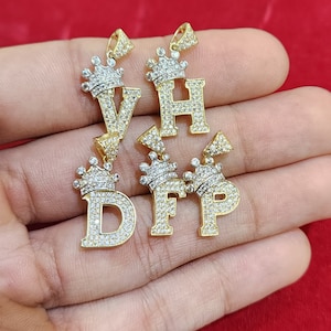 May include: Five gold pendants with a crown design and a letter in the center. The letters are V, H, D, F, and P. The pendants are covered in clear cubic zirconia stones.