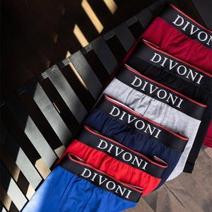 Può includere: Boxer assortiti in rosso, nero, grigio, blu navy e blu. Ogni paio presenta un elastico nero con la scritta bianca "DIVONI" e un bordo rosso. La biancheria intima è disposta su una superficie di legno scuro.