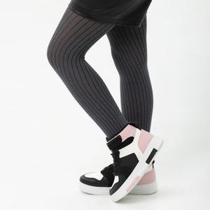 May include: Dark grey ribbed tights worn with high-top trainers featuring a colour-blocked design in black, white, and soft pink. The trainers include a hook-and-loop strap across the ankle and a thick white rubber sole with a textured heel detail.