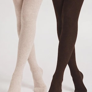 May include: A pair of over-the-knee socks in a light beige heathered knit and a pair of over-the-knee socks in a solid dark brown knit. Both pairs feature a ribbed cuff at the top and a soft, opaque texture that extends from the foot to the thigh.