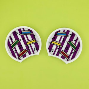 May include: A pair of purple and white striped earbud holders with musical notes and colorful stacked hats.