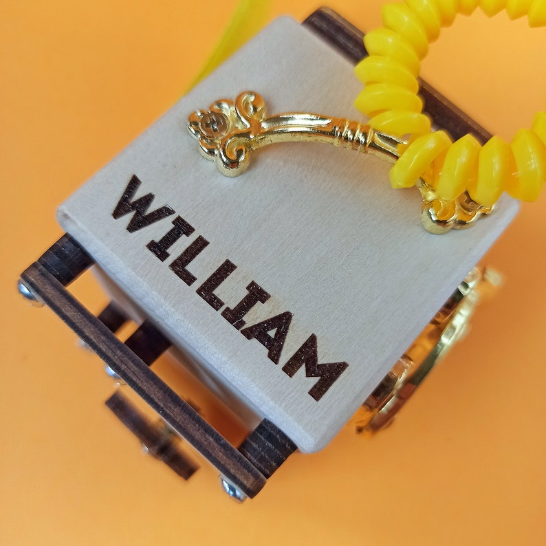 May include: A wooden box with a gold handle and a yellow coiled cord. The box is engraved with the name "WILLIAM".
