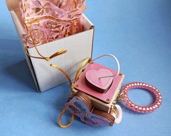 May include: A wooden box with a pink heart cutout and a butterfly design. The box is attached to a pink beaded bracelet and a white string. The box is sitting on a blue surface.