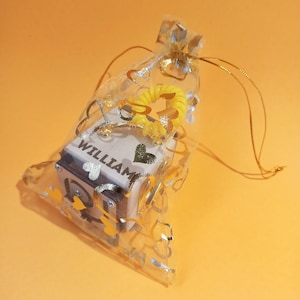 May include: A small wooden box with the name "William" engraved on it, inside a sheer gold and white heart-shaped bag with a yellow heart-shaped ribbon.