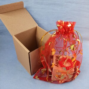 May include: A small wooden box with the word "Wally" printed on it, wrapped in a red sheer bag with gold hearts and floral designs. The box is sitting inside a brown cardboard box.