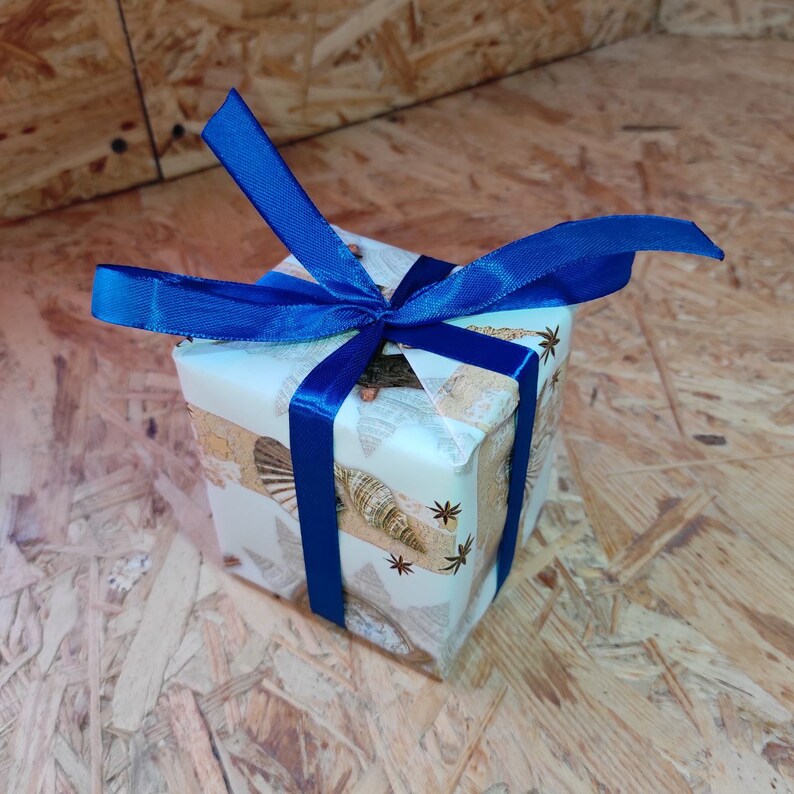 May include: A small gift box wrapped in white paper with a seashell pattern and tied with a blue ribbon.