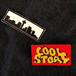 May include: Two embroidered patches. One is white with a black silhouette of a city skyline. The other is red with the words "COOL STORY" in yellow.