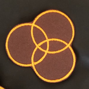 May include: A brown fabric patch with three interlocking circles outlined in orange thread.