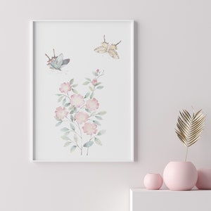 Op de afbeelding: Een ingelijste aquarelprint met roze bloemen en twee vlinders. De vlinders hebben blauwe en bruine vleugels. De bloemen hebben groene bladeren en stelen. De print zit in een witte lijst.