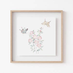 Op de afbeelding: Ingelijste aquarelprint met roze bloemen en vlinders. De vlinders zijn lichtblauw en beige, en de bloemen zachtroze. Het kunstwerk staat tegen een witte achtergrond.
