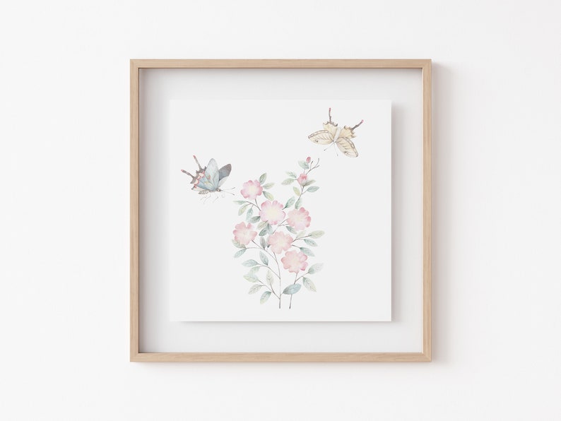 Op de afbeelding: Ingelijste aquarelprint met roze bloemen en vlinders. De vlinders zijn lichtblauw en beige, en de bloemen zachtroze. Het kunstwerk staat tegen een witte achtergrond.