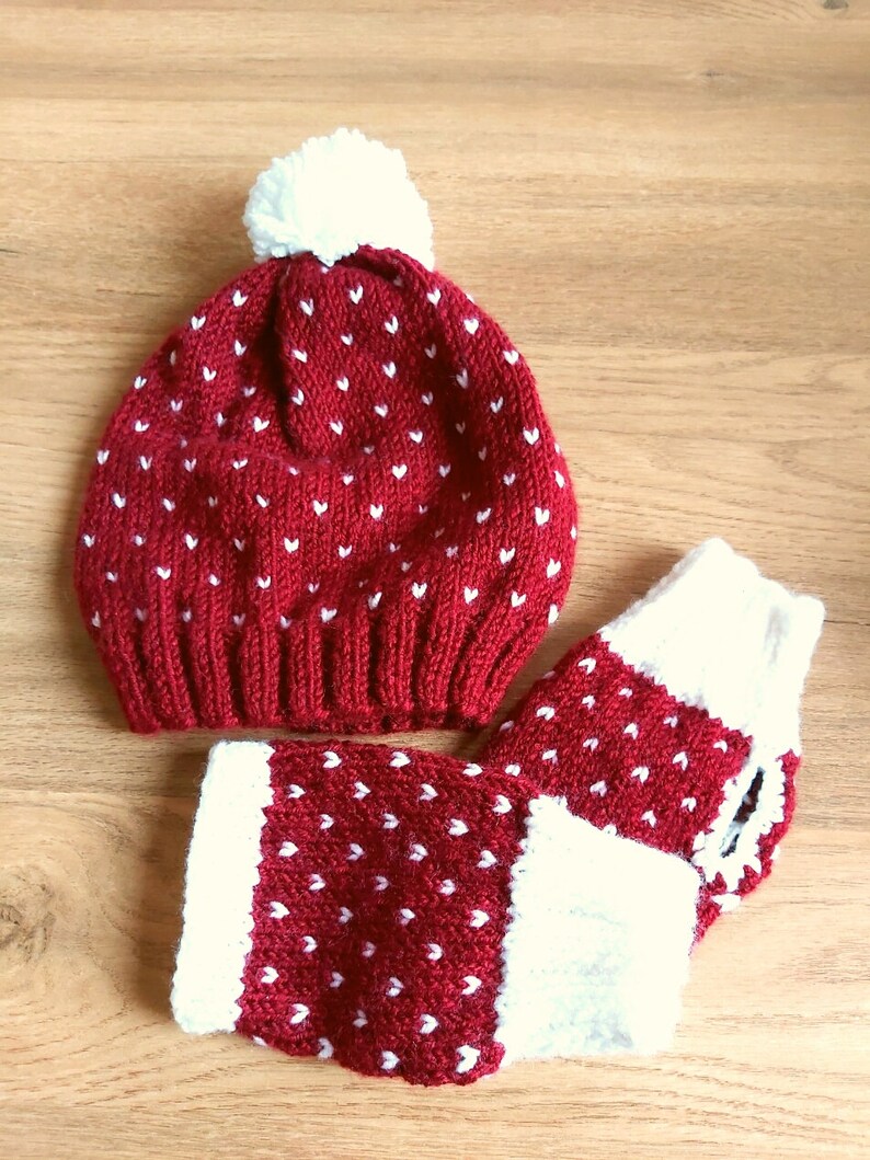 May include: Red knitted hat with white pom pom and white heart pattern. Matching red and white knitted fingerless gloves with white heart pattern.